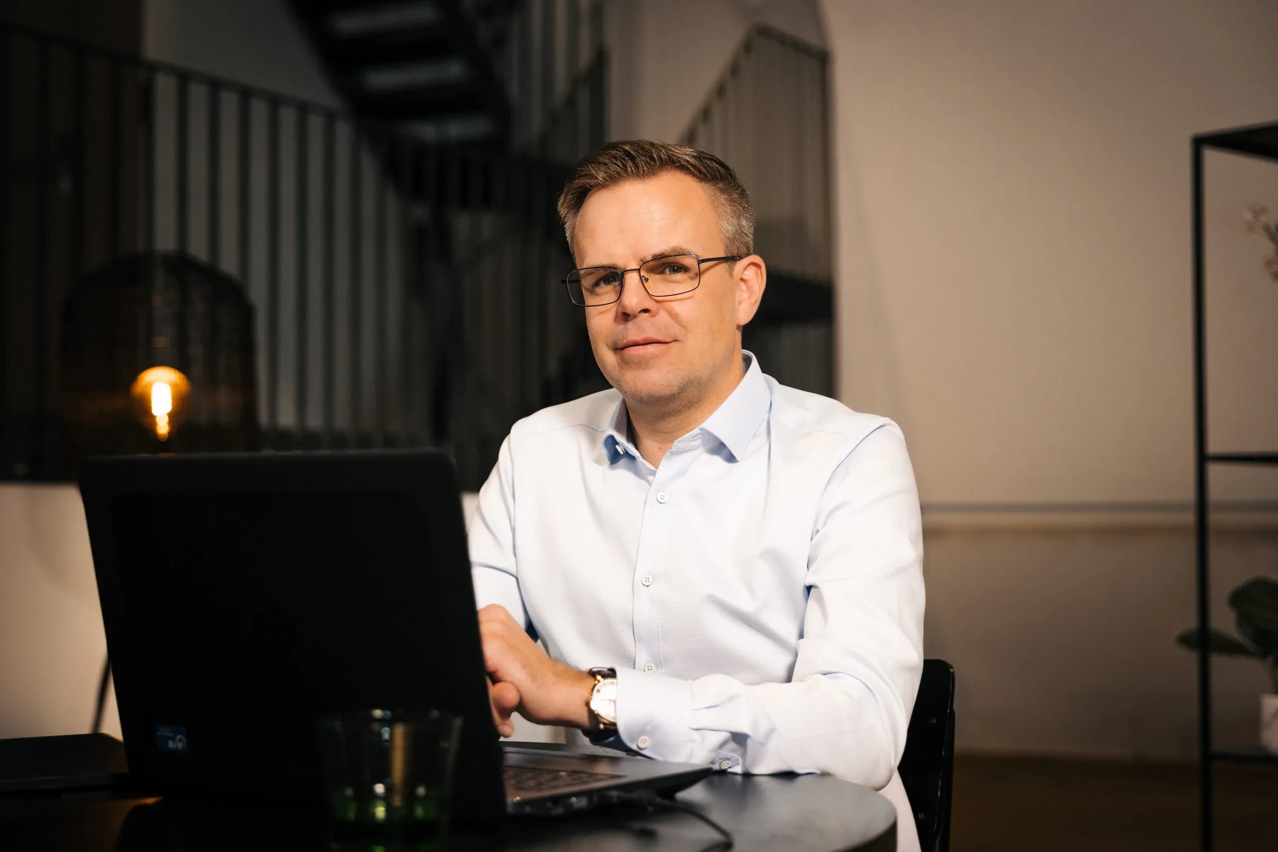 Berater sitzt am Laptop im Loft-Büro und blickt in die Kamera